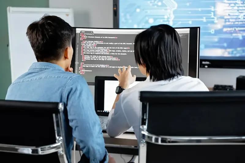Two students writing code on large monitors