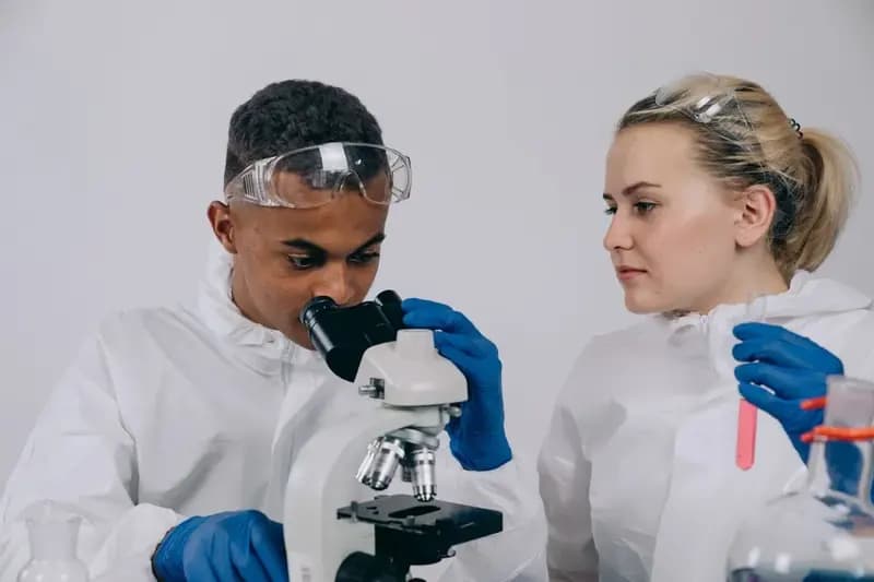Two students in lab coats working with a microscope in a laboratory