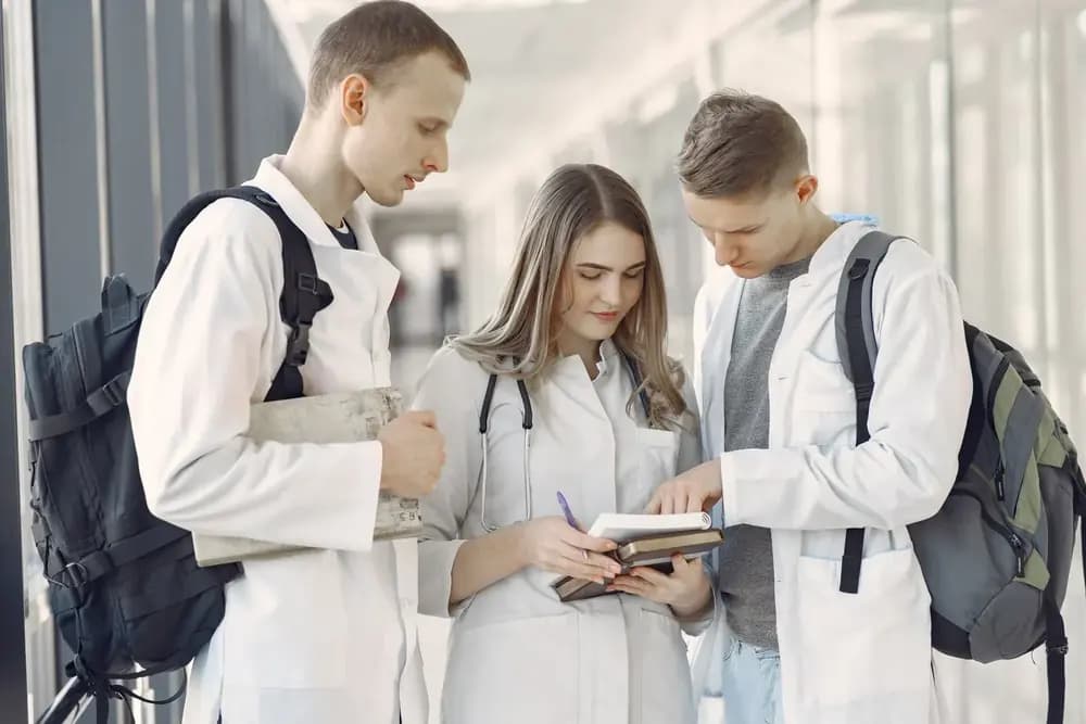 Three medical students in white coats reviewing notes together in a hallway
