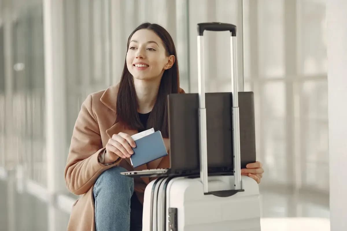 Traveller with a passport and suitcase checking travel details on a laptop at the airport