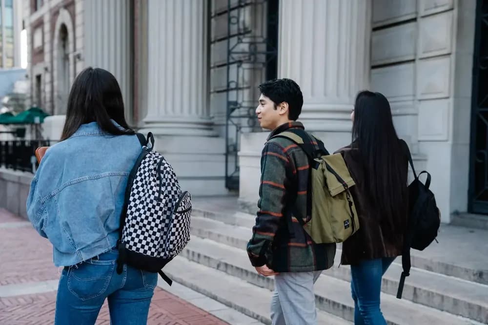 Three students with backpacks walking past a historic building in the city